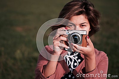 Girl photographer with mirrorless camera like old camera looks to the camera with a green background Stock Photo