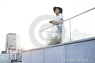 Girl photographer, photographs the city on the roof of the house, a woman tourist looks from the balcony of the hotel at sunset Stock Photo