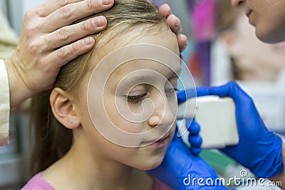 Girl pierced ear in the beauty salon. Adorable little girl having ear piercing process with special equipment in beauty center by Stock Photo