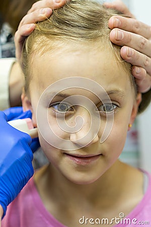 Girl pierced ear in the beauty salon. Adorable little girl having ear piercing process with special equipment in beauty center by Stock Photo