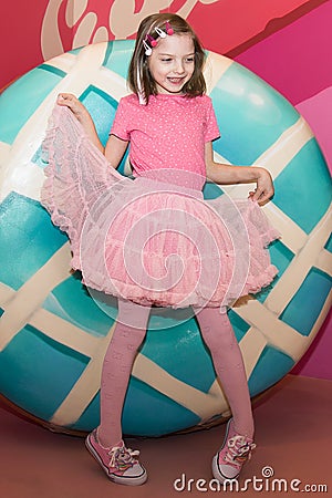 Girl in pink clothes with a Lollipop. In the background, a variety of sweets. Stock Photo