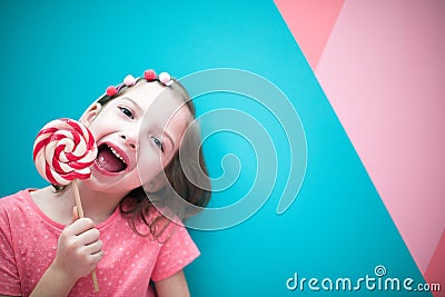 Girl in pink clothes with a Lollipop. In the background, a variety of sweets. Stock Photo