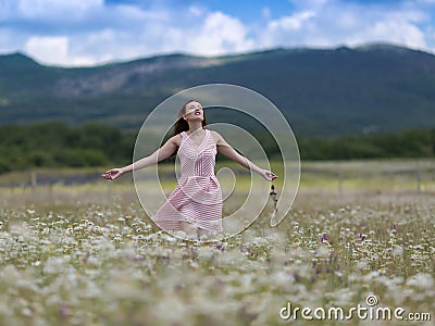 Girl in pink sleeveless dress walks on meadow of chamomile Stock Photo
