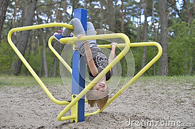 A girl is playing on the playground on the yellow metal attraction. It's windy. Stock Photo