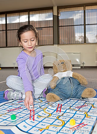 Girl Playing Snakes and Ladders with Teddy Bear. Stock Photo