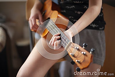 The girl plays the four-stringed guitar. Lesson playing ukulele. Love for music. Acoustic tool. Hands of a girl on the bar. Stock Photo