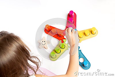 A girl plays a game with colored wooden blocks. Sorter. The development of size, color. Stock Photo