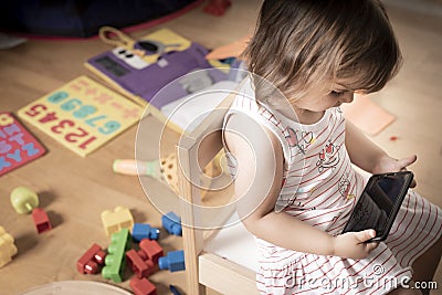 Girl Plays Mobile Phone. The Girl is Hooked to the Mobile Phone. He does not play with toys. The mobile phone is bad for children Stock Photo