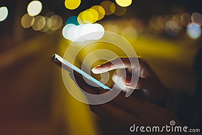 Girl pointing finger on screen smartphone on background illumination glow bokeh light in night atmospheric city, hipster using Stock Photo