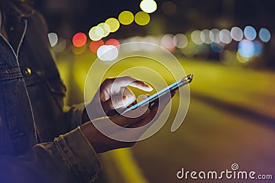 Girl pointing finger on screen smartphone on background illumination glow bokeh light in night atmospheric city, hipster using Stock Photo