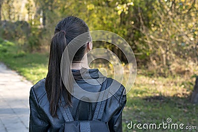 Girl with ponytail is walking in the park. Young girl student stands in the park. Back view Stock Photo