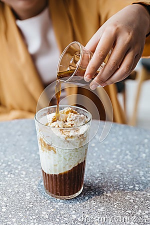 A girl is pouring a shot of espresso in frozen milk mixed with coffee jelly on granite top table. Stock Photo