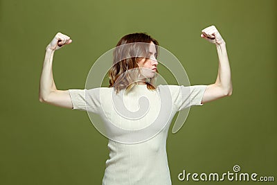 Girl power. Confident proud strong independent young woman showing arms muscles, demonstrate biceps on green background Stock Photo