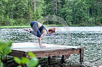 Girl practicing yoga, doing Bakasana exercise, Crane pose, on the lake. Concept of healthy life and natural balance Stock Photo