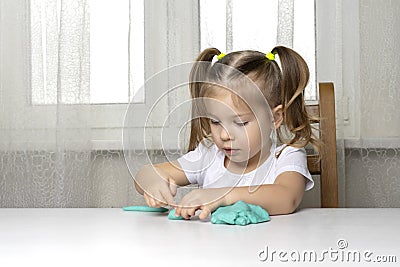 Girl preschooler sits at a table and sculpts from turquoise dough for modeling Stock Photo