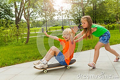 Girl pushes boy with arms apart on skateboard Stock Photo