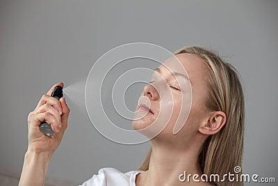 The girl puts the foundation under the makeup of the spray on the face. Stock Photo