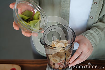 The girl puts the sliced kiwi in a blender Stock Photo