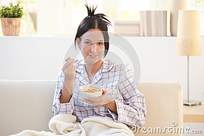 Girl in pyjama having cereal breakfast on couch Stock Photo