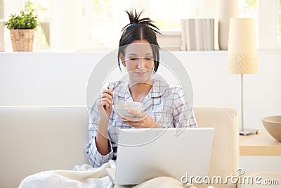 Girl in pyjama having cereal using laptop Stock Photo