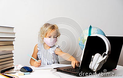 A girl in quarantine wearing a mask with a laptop is undergoing school training remotely Stock Photo