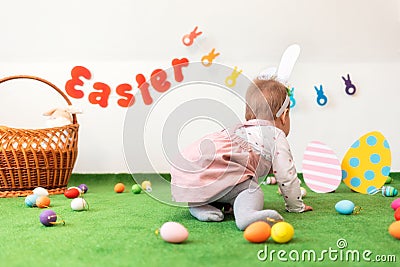 A girl with rabbit ears, sitting on an artificial lawn looking at the background with eggs. Rear view. Easter concept Stock Photo