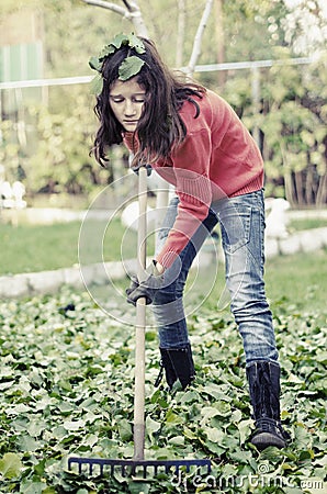 Girl with a rake tool cleaning garden green leafs Stock Photo