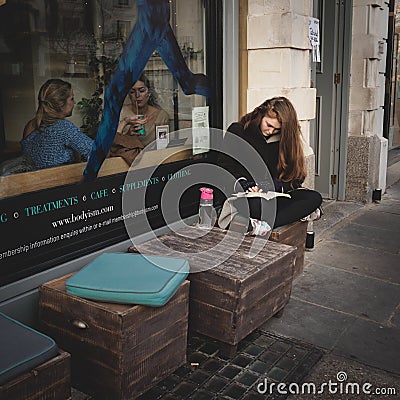 Girl reading a book outside a cafÃ¨ in Notting Hill. London UK. March 2017. Squared format Editorial Stock Photo