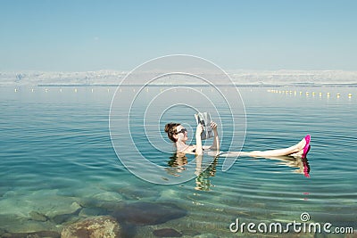 Girl reading newspaper floating on surface Dead Sea enjoy summer sun and vacation. Recreation tourism, healthy lifestyle, free tim Stock Photo