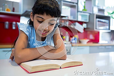 Girl reading novel with arms crossed in kitchen Stock Photo