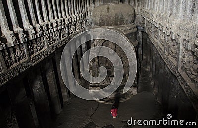 A girl in a red dress is sitting at the feet of the Buddha and praying. There is a very grand and linear statue of Buddha, Ellora Stock Photo