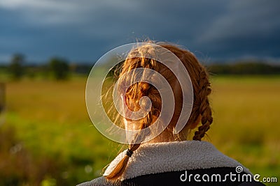 Girl With Red Hair in Braids Walks Through a Field in the Countryside Stock Photo