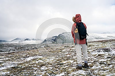Girl with red hooded jacket and backpack are hiking in snow covered mountains with beautiful scenic landscape view and foggy weath Stock Photo