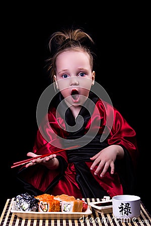 Girl in a red kimono before a plate with rolls Stock Photo