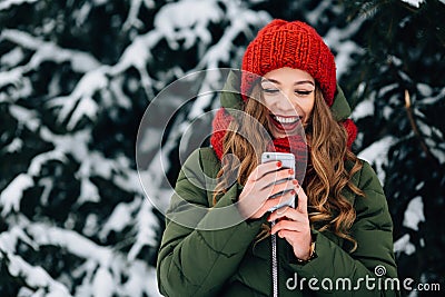 Girl in red winter hat and scarf using smartphone and smiling. Stock Photo