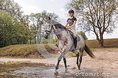 Girl riding gray horse down the calm river water Stock Photo