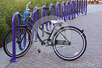 Girl`s bicycle anchored with safety chain to purple bike rack Stock Photo