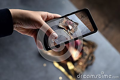 Girl`s hand shoots food dessert on the phone. chocolate pudding cake filled with fresh berries on the Golden tray with folk and Stock Photo