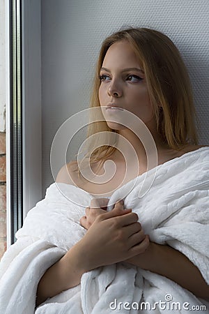 Girl is sad at the window wrapped in a cozy blanket Stock Photo