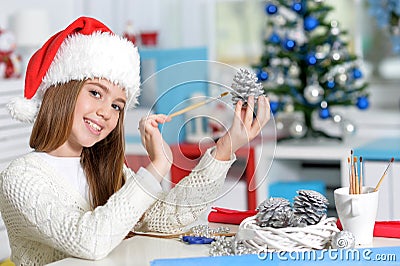 Girl in Santa hat preparing for Christmas paintig pine cone Stock Photo