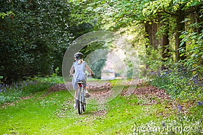 Girl in school uniform and cycle helmet riding bike along a tree lined country track Stock Photo