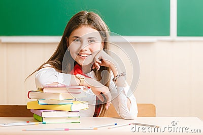 Girl in school uniform sitting at her desk in the classroom with books. Student in class at school Stock Photo