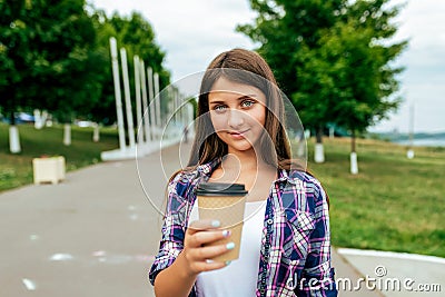 A girl schoolgirl, 13-16 years old, stands summer in city in hand cup with a coffee tea drink. Free space for text Stock Photo