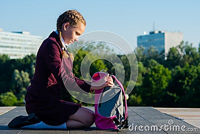 girl of the senior classes, takes out textbooks from a pink backpack in the open air Stock Photo