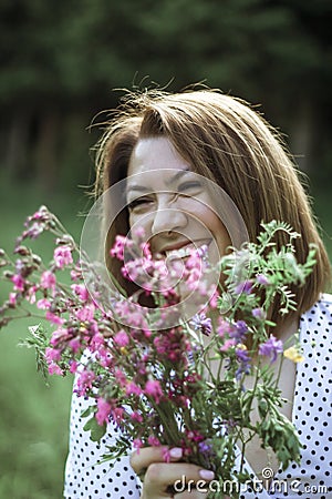 A girl with a short haircut laughs and hides behind flowers. A close portrait of a young beautiful woman in a meadow with lilac Stock Photo