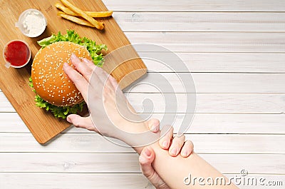 The girl shows willpower by holding with her left hand, her right hand that reaches for a hamburger. Diet and healthy nutrition, Stock Photo