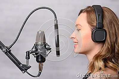 Girl sings into a microphone, in headphones in a studio. Producing and creating songs, music, recording a track. Writing an album Stock Photo