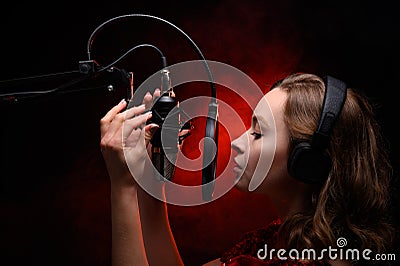 Girl sings in a red dress and red backlight. Microphone in a recording studio. Effective background. Vocal. Vocal schools and Stock Photo