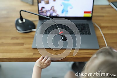 Girl sit on chair and play in online game with laptop and microphone on table at home. Stock Photo