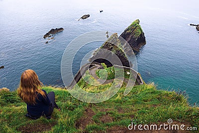 Girl sits on a cliff over the ocean in Ireland Stock Photo